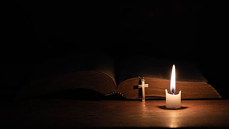 Kerze neben einer Bibel und einem Kreuzanhänger