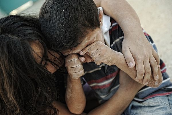 Fluechtlingsjunge weint und wird von seiner Mutter umarmt