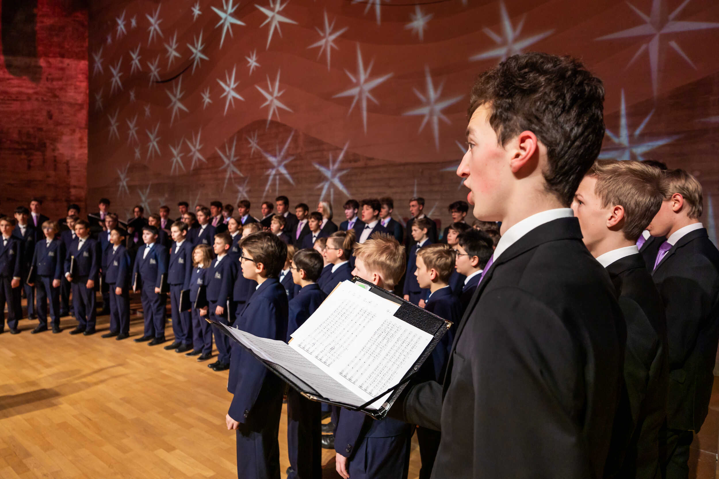 Junger Sänger mit Liederheft im Vordergrund des Domspatzenchors beim Singen