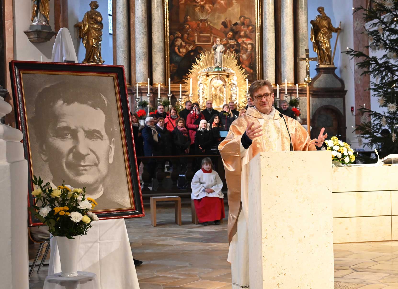 Priester predigt neben Foto von Don Bosco