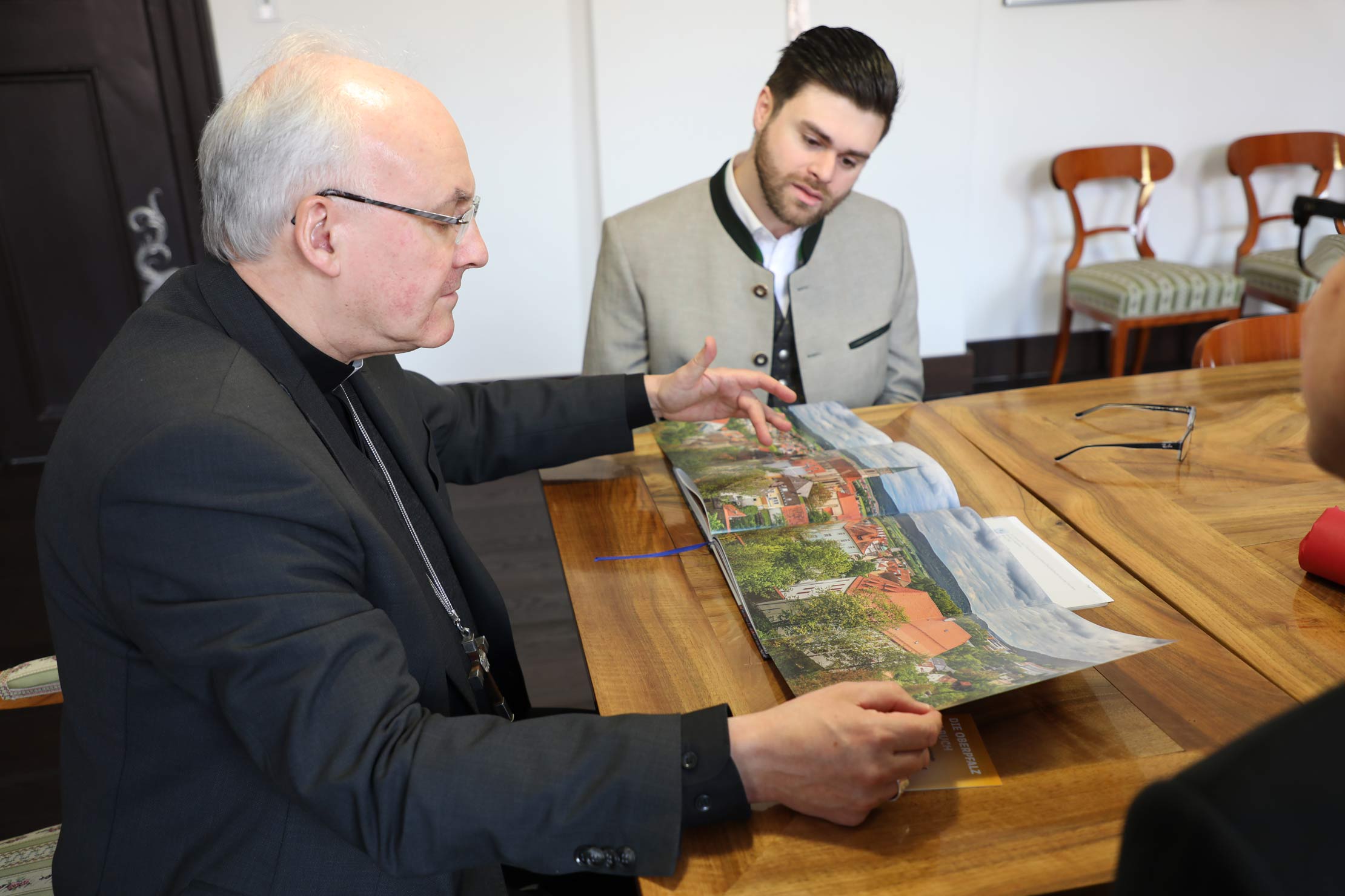 Bischof und junger Mann in bayerischer Tracht betrachten einen Bildband