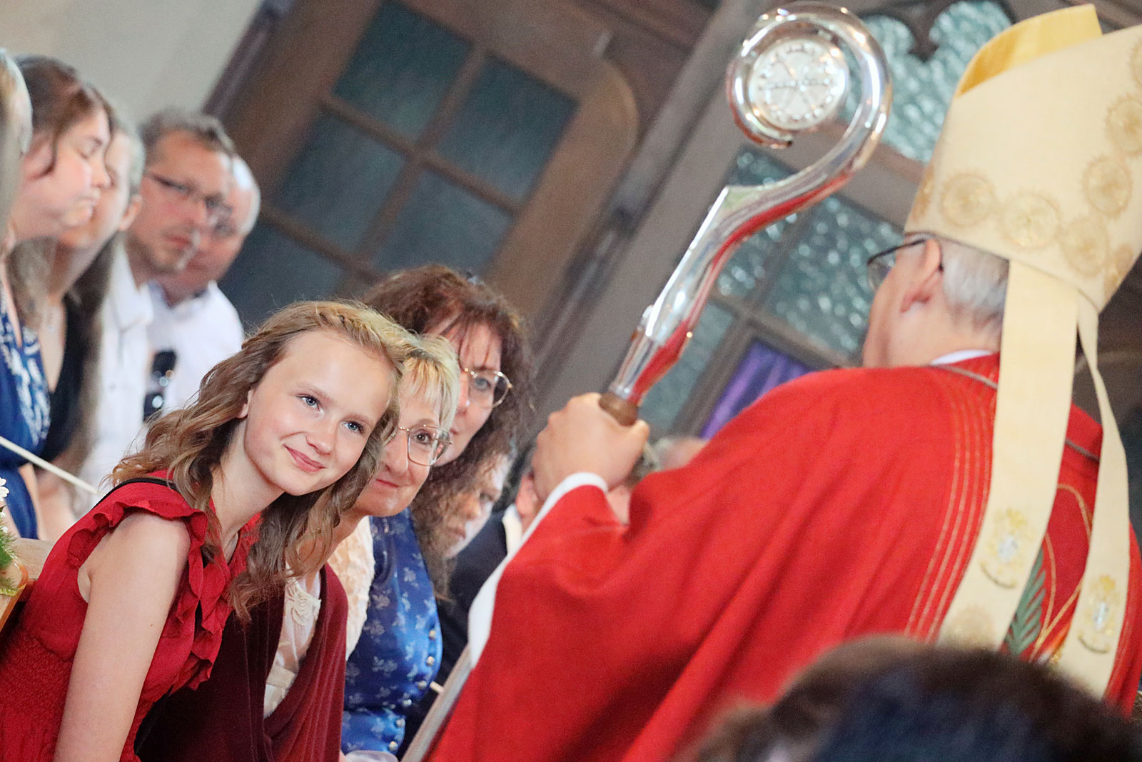 Mädchen hört zusammen mit ihrer Patin lächelnd dem Bischof bei der Predigt zu