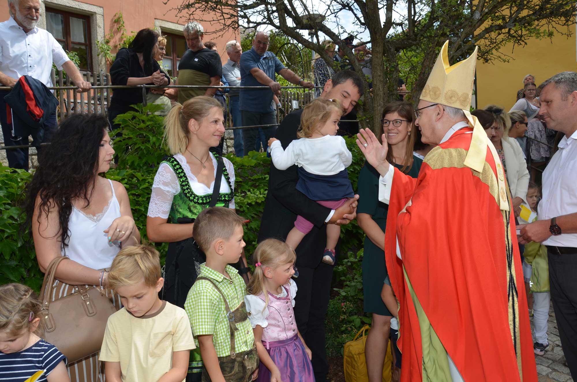 Bischof segnet Kind, umringt von vielen Leuten