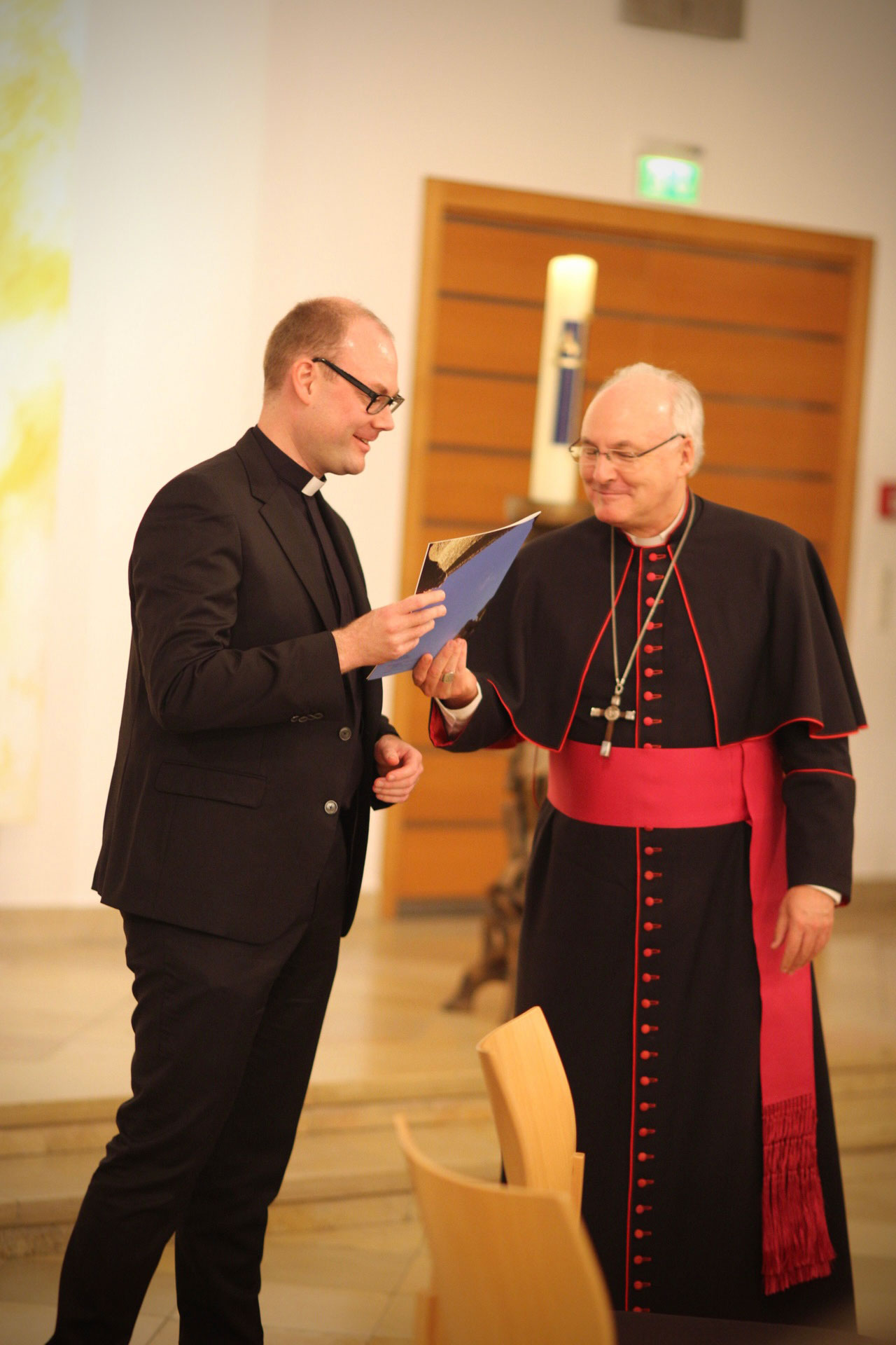 Bischof übergibt Urkunde an einen jungen Priester