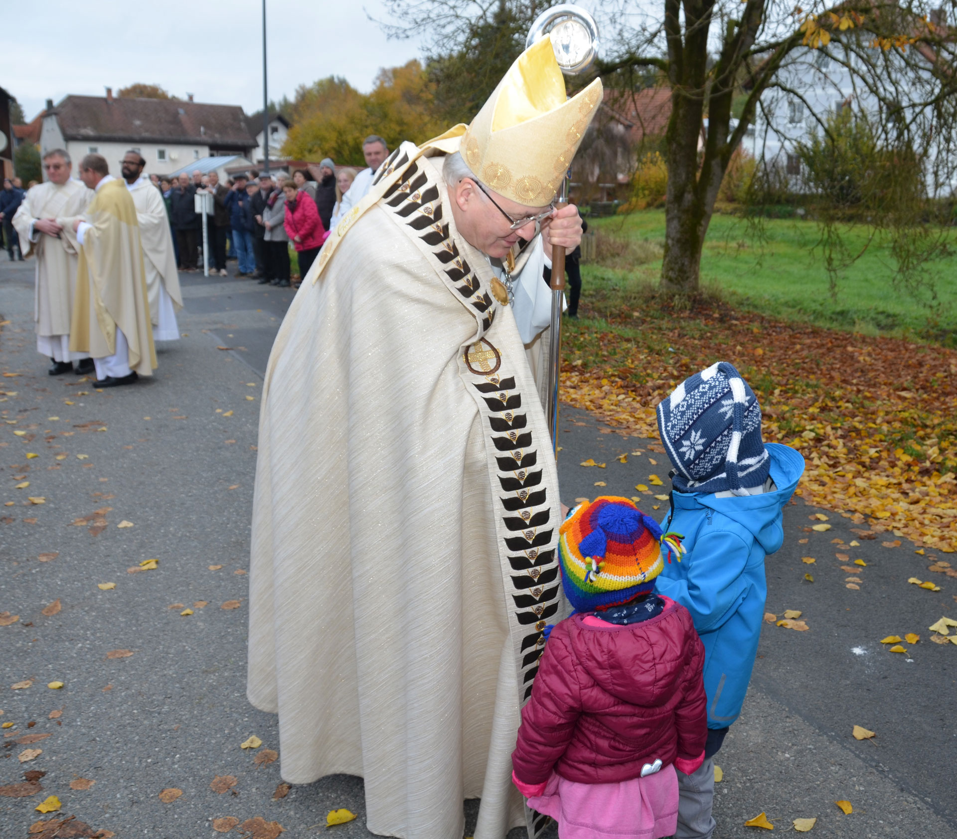 Bischof segnet zwei Kinder auf herbstlicher Straße