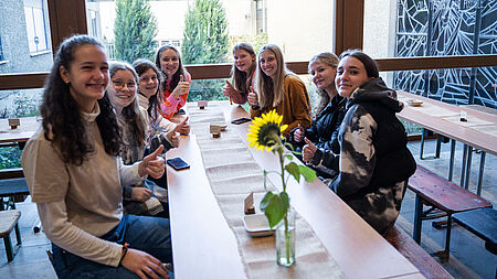 Junge Mädchen sitzen an einem Tisch und lächeln.