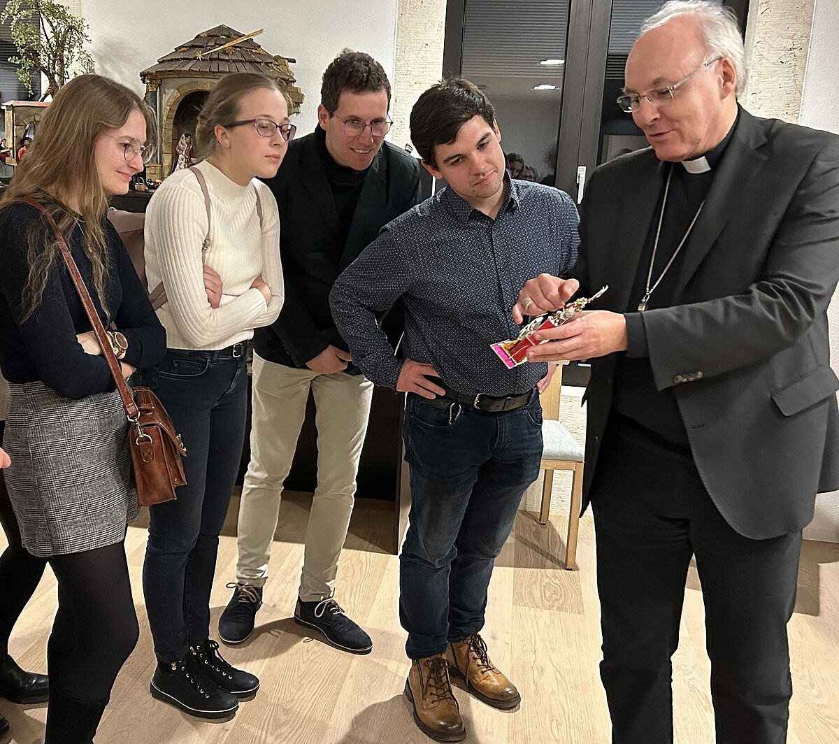 Junge Leute lassen sich interessiert vom Bischof eine Krippe erklären