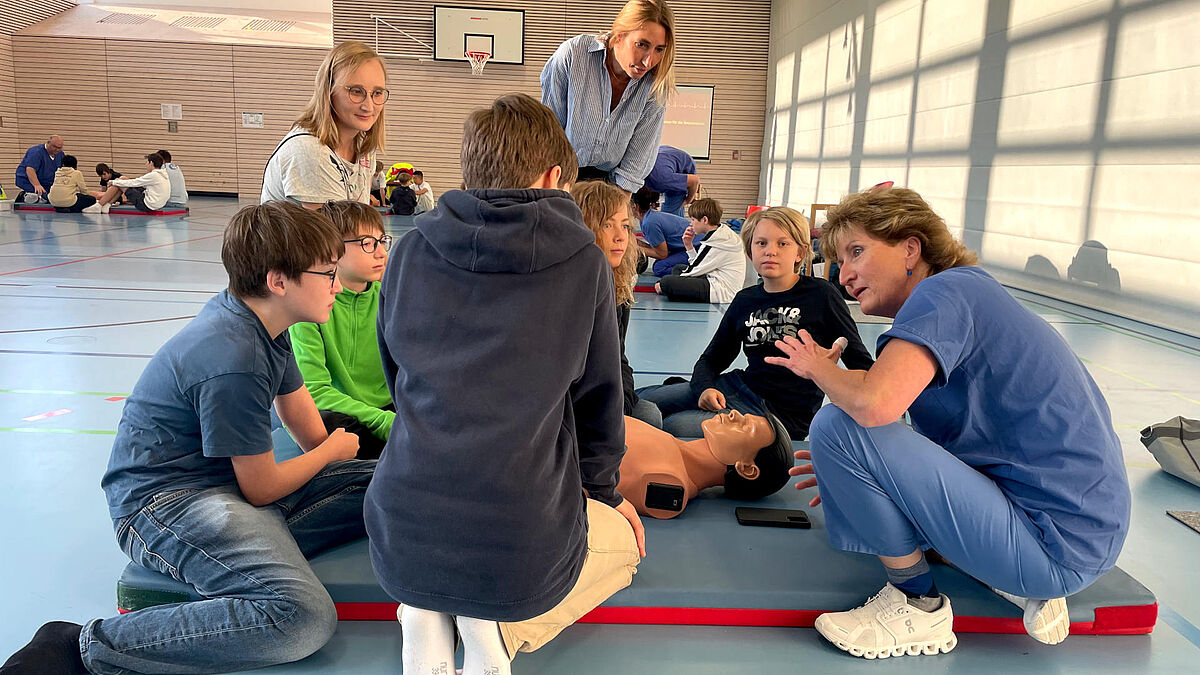 Notärztin erklärt Schülern in einer Turnhalle lebensrettende Sofortmaßnahmen an einer Puppe