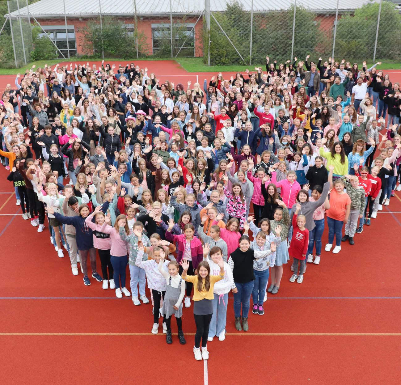 Viele Schüler in Herzform aufgestellt auf einem Sportplatz