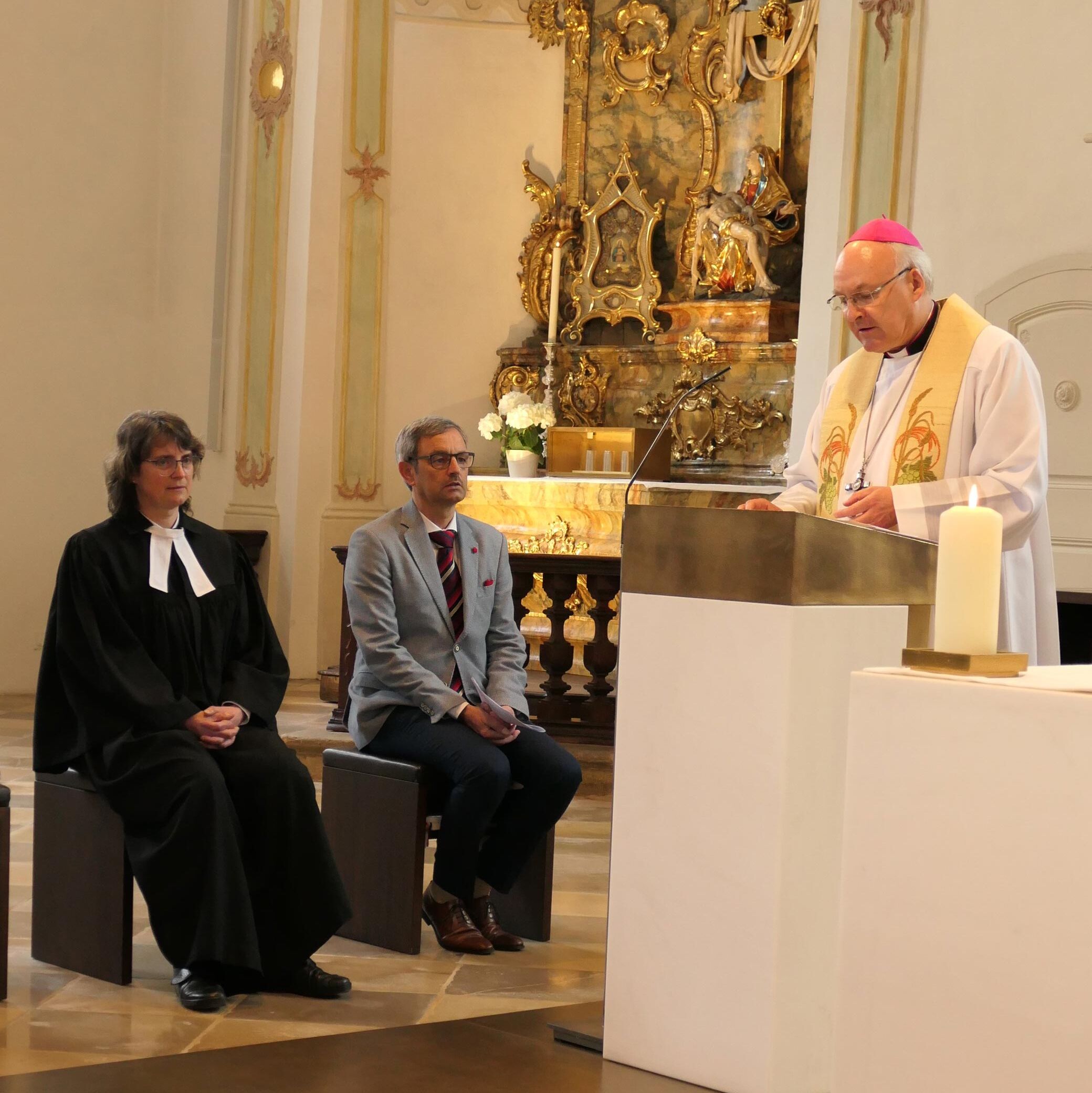 Bischof bei Predigt neben zwei Gästen