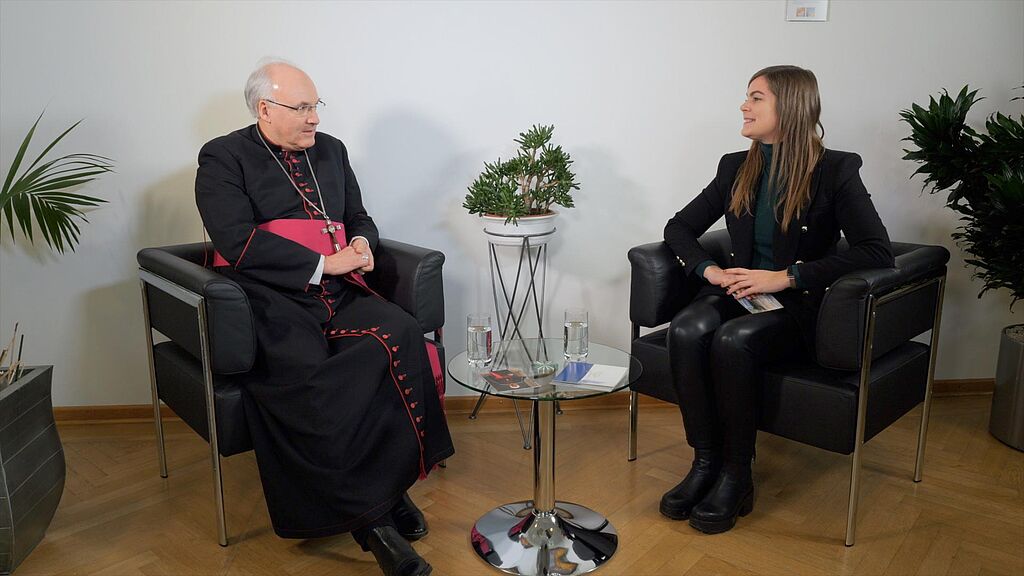 Bischof und junge Moderatorin in schwarzen Sesseln gegenüber im Gespräch