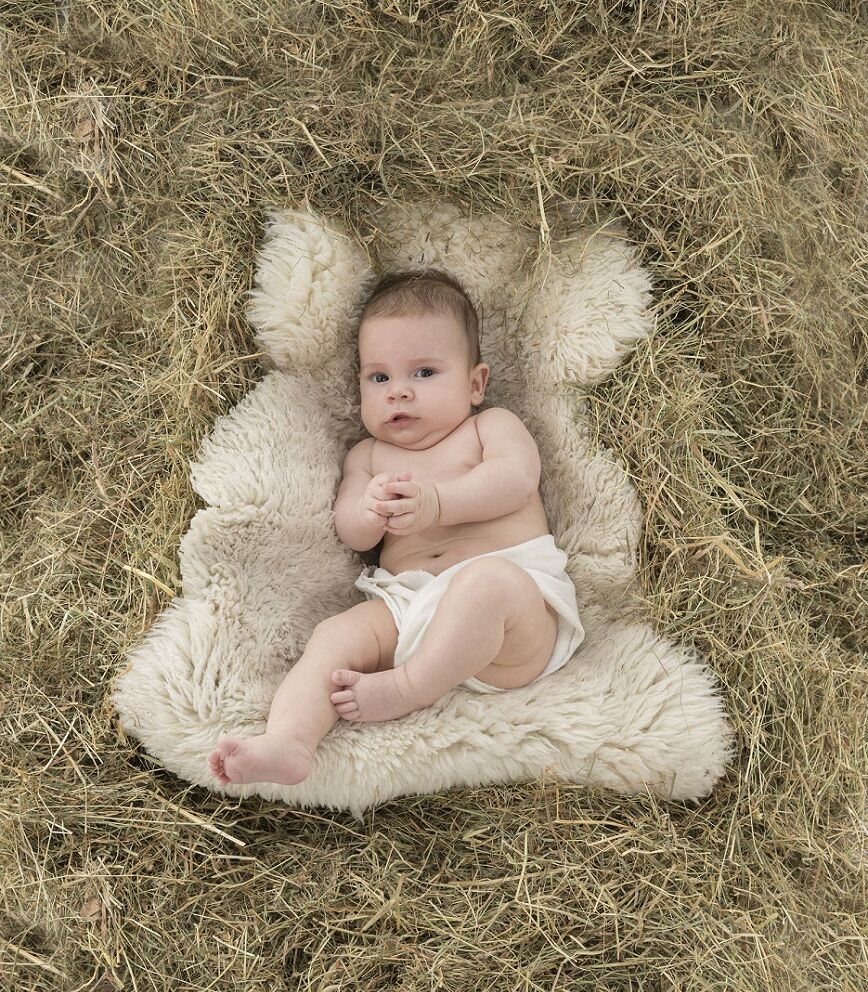 Baby auf Schaffell liegend inmitten von Stroh