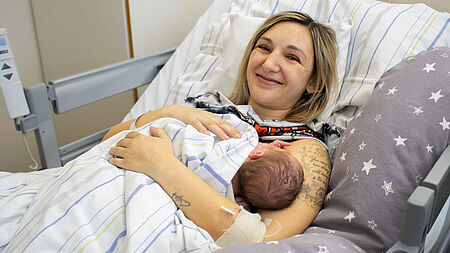 Glückliche Mutter hält ihr Neugeborenes im Krankenhausbett