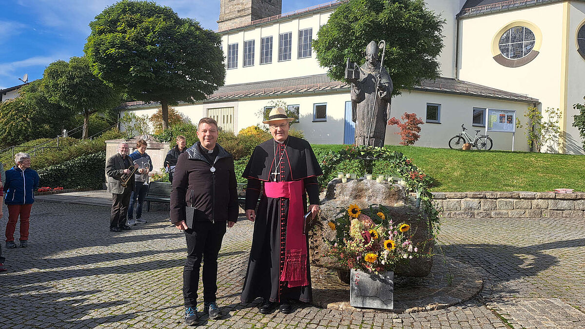 Bischof und ein Mann vor eine Heiligenstatue von Wolfgang