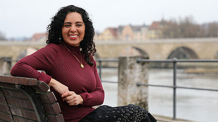 Eine junge Frau sitzt auf einer Bank an der Donau.