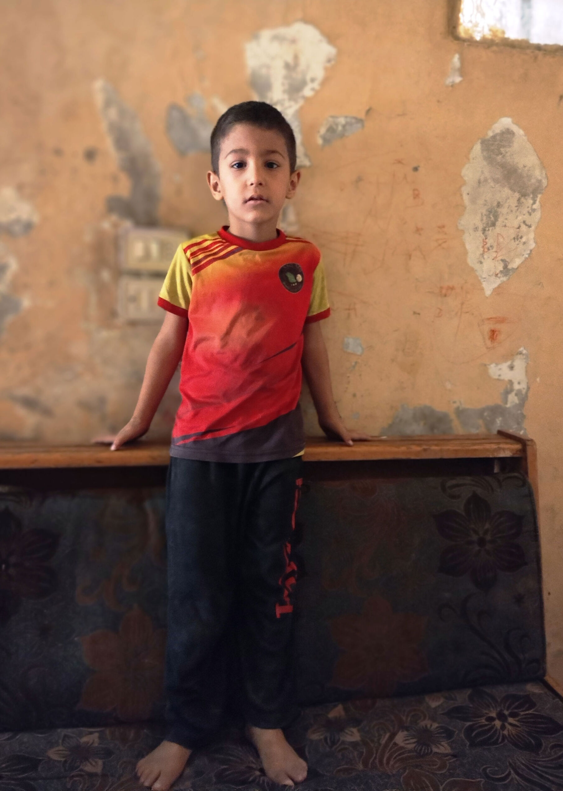 Kleiner syrischer Junge vor kaputter Wand