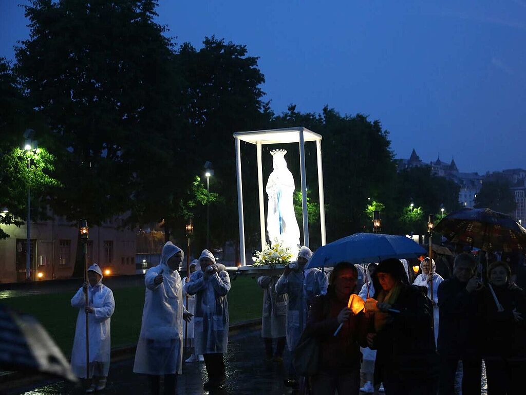 Kerzenprozession mit Madonnenstatue in Lourdes im Dunkeln bei Regen 
