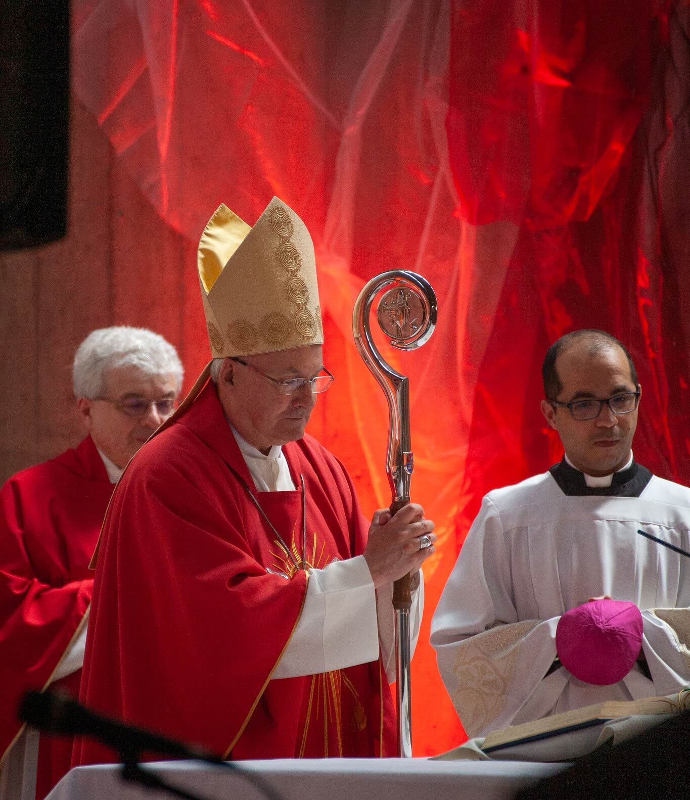 Bischof am Altar vor rot beleuchtetem Hintergrund, sehr stimmungsvoll