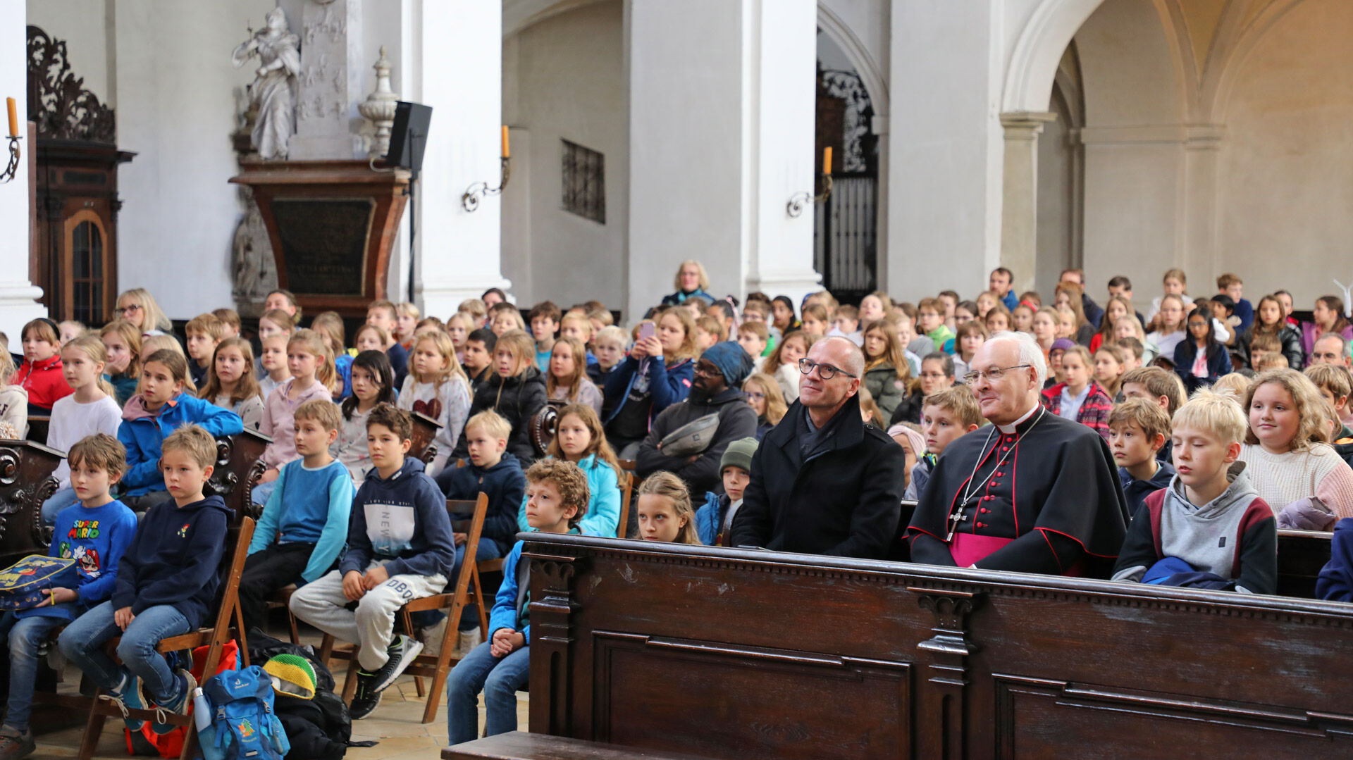 Bischof Rudolf und Stadtdekan Gerl genießen die Vorstellung inmitten der Schulkinder