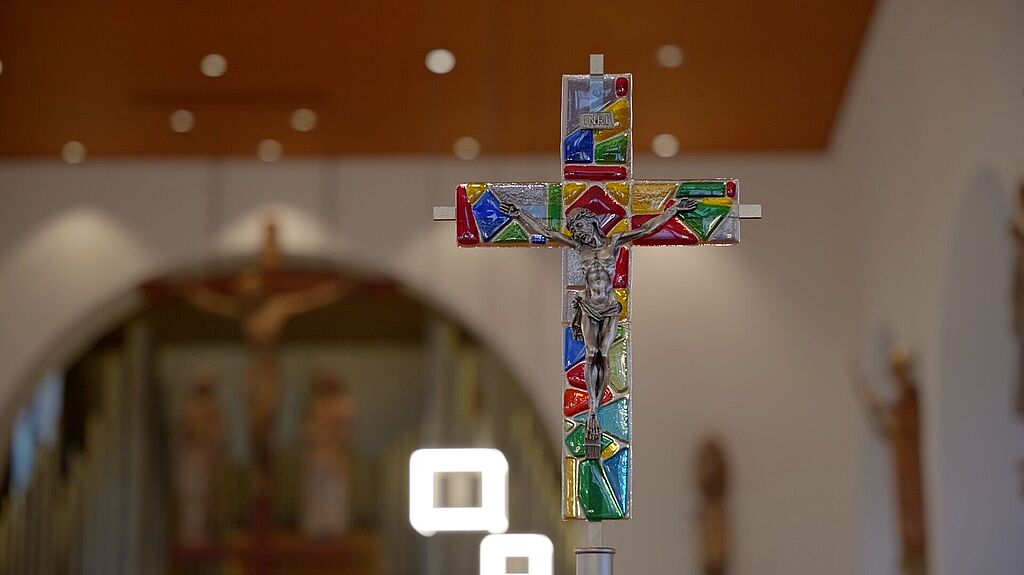 Ein bunt verziertes hängendes Kreuz in der Kirche St. Konrad in Regensburg.