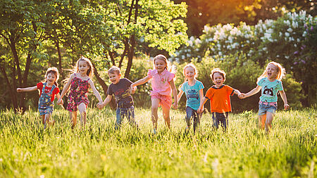 Kinder hüpfen sich an den Händen haltend über eine Sommerwiese