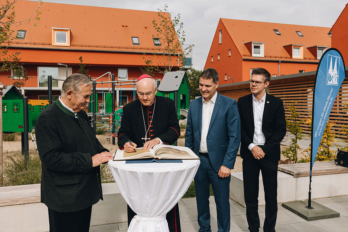 Bischof und drei andere Herren im Anzug vor einem Neubau