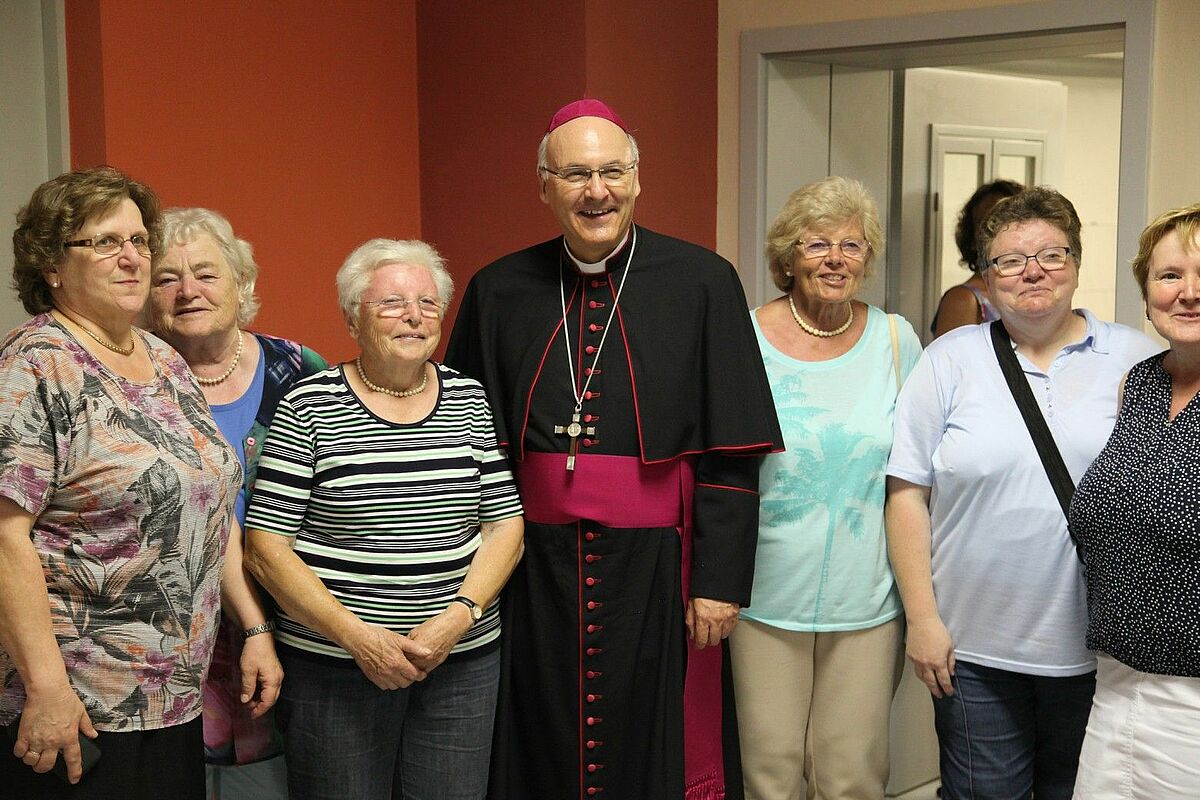 Mehrere ältere Frauen psoieren neben Bischof