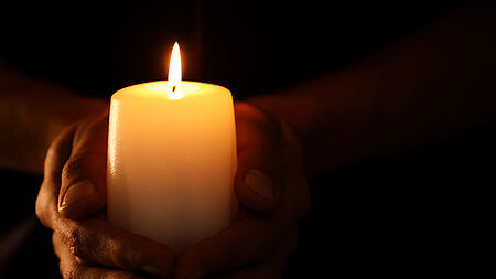 Hände halten brennende Kerze im Dunkeln