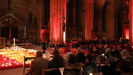 Nacht der Lichter im Regensburger Dom. Auf dem Foto ist der Dom St. Peter zu sehen. Auf dem Boden sitzen junge Leute und es stehen dort auch Kerzen.