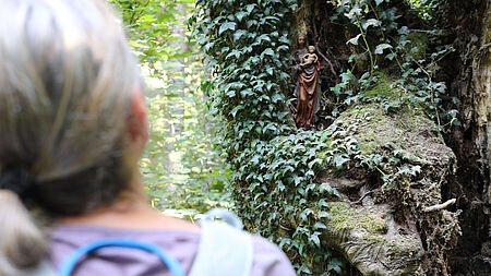 Der Zusammenhang von Glaube und seelischer Gesundheit: Eine Frau findet Trost bei einer Muttergottesstatue im Wald.