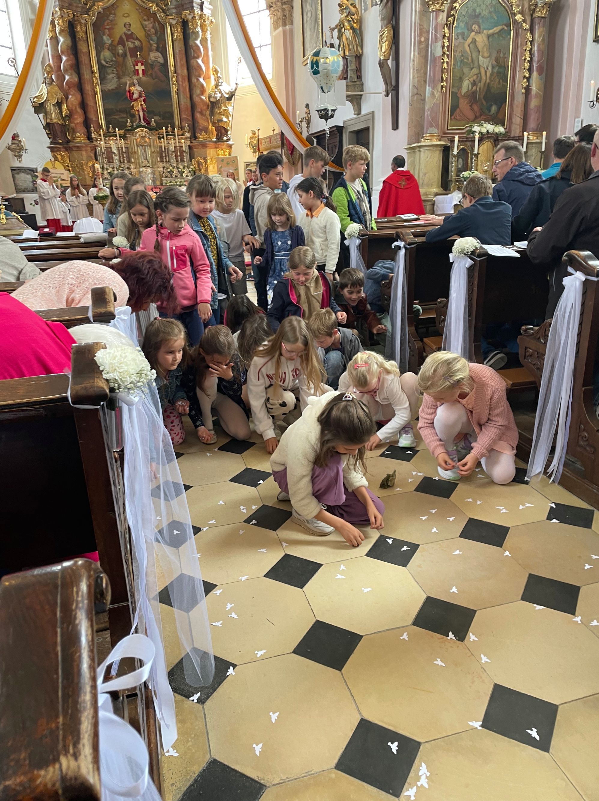 Kinder sammeln beim Pfingstgottesdienst die weißen Papiertauben vom Kirchenboden