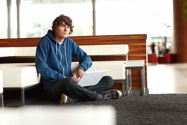 Jugendlicher sitzt vor Couch mit Laptop am Boden
